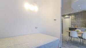 A modern bedroom with a single bed, a small desk, and a kitchenette in the background. - JOIVY Cosy & Modern Apartments near Milan Central Station (Milan)