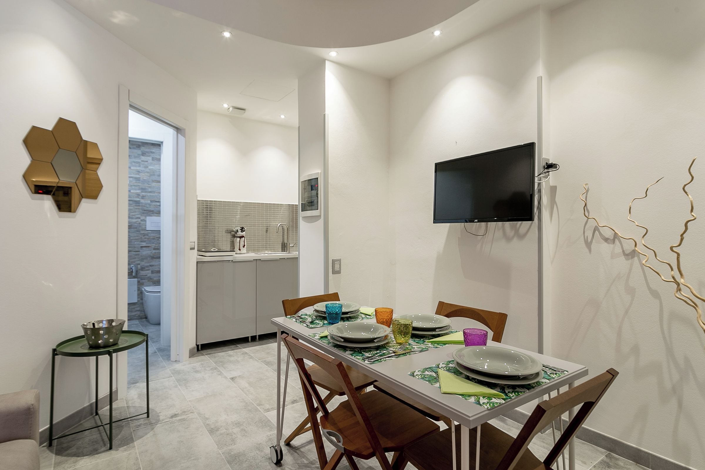 Una cocina moderna con lavavajillas integrado, un comedor con una mesa dispuesta para cuatro personas y un televisor de pantalla plana montado en la pared.