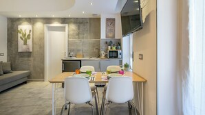 A modern kitchen with a dining area, featuring a wooden table, white chairs, and a flat-screen TV mounted on the wall. - JOIVY Cosy & Modern Apartments near Milan Central Station (Milan)