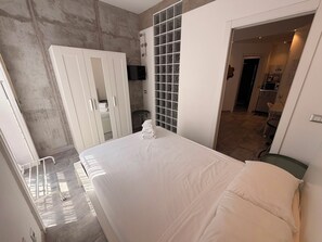 A bedroom with a bed, a wardrobe, a bathroom with a glass shower, and a kitchenette. - JOIVY Cosy & Modern Apartments near Milan Central Station (Milan)