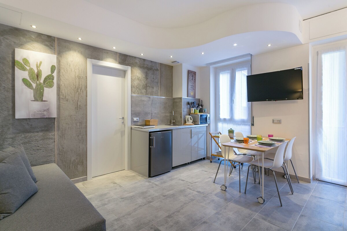 A modern kitchen with a built-in oven, microwave, and refrigerator. There is a dining area with a table and chairs, and a flat-screen TV mounted on the wall.