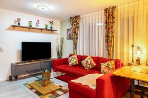 A modern living room with a red sofa, a flat-screen TV, a glass coffee table, and a wooden side table.