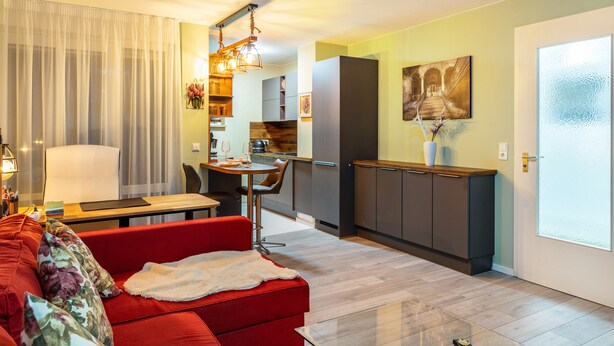 Un salon moderne avec un canapé rouge, une table à manger et un coin cuisine équipé de placards et d’un réfrigérateur.