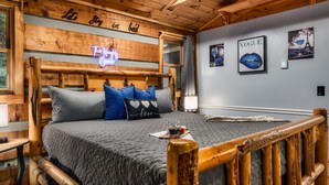 Un dormitorio tipo cabaña de madera con una cama, almohadas, un letrero de neón y decoración en la pared.