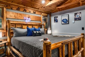 Una camera da letto in stile baita con un letto, cuscini, un cartello luminoso al neon e decorazioni alle pareti.
