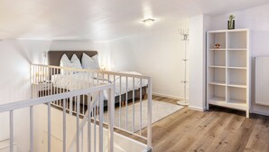 A bedroom with a bed, a white crib, a white shelving unit, and a radiator. - Maisonette Apartment near BER Airport, Schönefeld – 2 Bedrooms, Parking, Wi-Fi (Schönefeld)