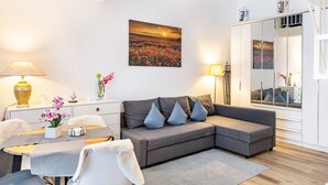 A modern living room with a grey sofa, a dining table, and a large window. - Maisonette Apartment near BER Airport, Schönefeld – 2 Bedrooms, Parking, Wi-Fi (Schönefeld)