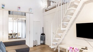 A modern living room with a grey sofa, a staircase, a flat-screen TV, and a large window. - Maisonette Apartment near BER Airport, Schönefeld – 2 Bedrooms, Parking, Wi-Fi (Schönefeld)