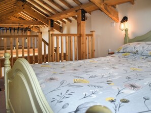 A bedroom with a wooden ceiling, a bed with floral bedding, and a nightstand with a lamp. - The Calving Barn - UK49679 (Bratton Fleming)