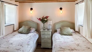 A bedroom with two single beds, a nightstand with a lamp, and a vase with flowers. - The Calving Barn - UK49679 (Bratton Fleming)