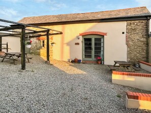 A rustic building with a stone exterior, a green door, and a gravel patio area with picnic tables.