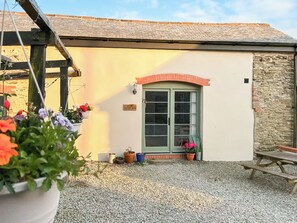A quaint cottage with a green door, a stone wall, and a gravel driveway.