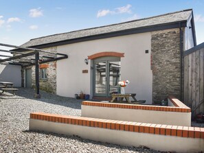 A building with a stone facade, a green door, and a small outdoor seating area with a table and chairs. - The Calving Barn - UK49679 (Bratton Fleming)