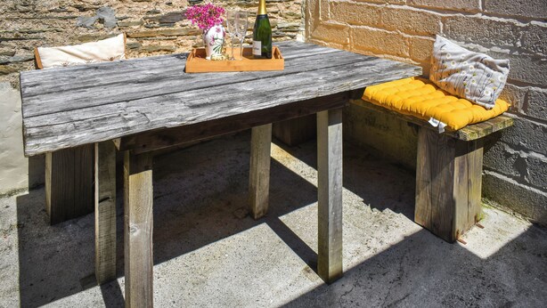 A rustic wooden table with a bench, a bottle of champagne, and a vase of flowers. - The Calving Barn - UK49679 (Bratton Fleming)