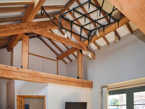 A room with exposed wooden beams, a ceiling light fixture, and a window with a view of greenery outside. - The Calving Barn - UK49679 (Bratton Fleming)