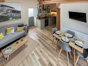 A modern living room with a grey sofa, a dining table set for four, and a kitchen in the background.