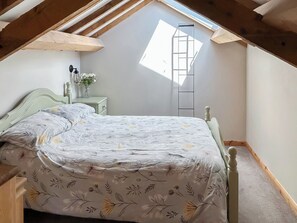 A bedroom with a sloped ceiling, a bed with a floral bedspread, a nightstand with a vase of flowers, and a skylight. - The Calving Barn - UK49679 (Bratton Fleming)