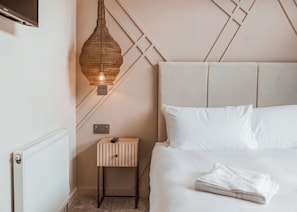 Une chambre à coucher comprenant un lit, une table de chevet avec une télécommande, un luminaire fixé au mur et un radiateur.