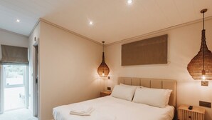 Un dormitorio con una cama grande, dos mesitas de noche, una lámpara colgante y vistas al exterior.