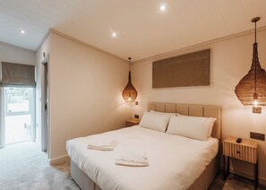 Un dormitorio con una cama grande, dos mesitas de noche, una lámpara colgante y vistas al exterior.
