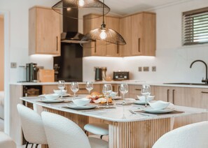 A modern kitchen with wooden cabinets, a central island with seating, and pendant lighting.