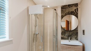 Un baño moderno con ducha envuelta en vidrio, espejo redondo y tocador de madera.