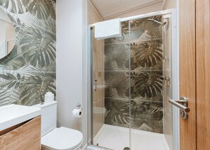 A bathroom with a glass shower enclosure, a toilet, and a sink.