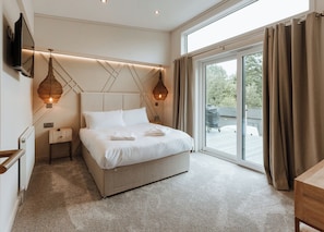 Un dormitorio moderno con una cama grande, un televisor montado en la pared y vistas al exterior a través de una puerta corrediza de vidrio.