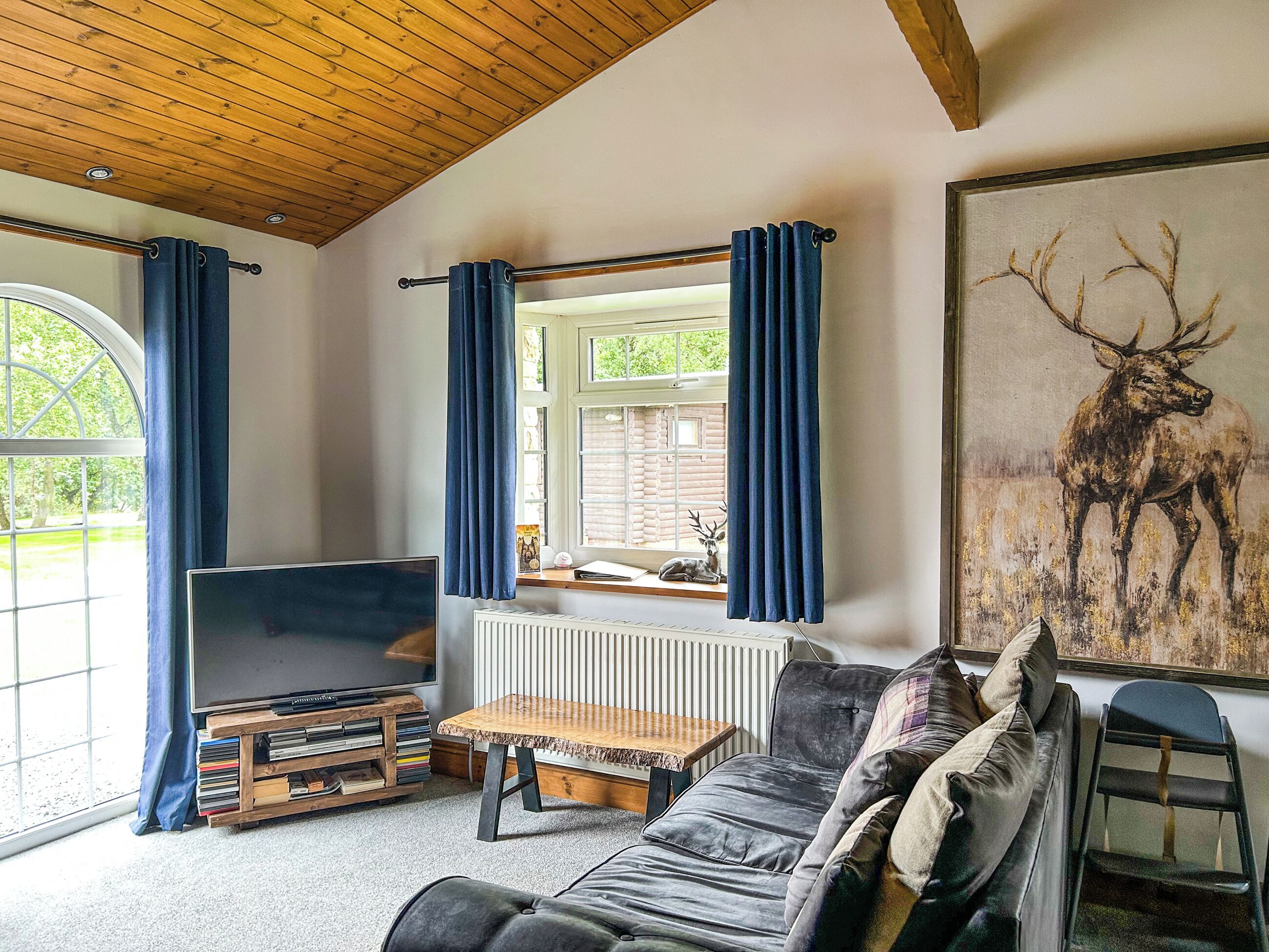 A living room with a TV, sofa, and a painting of a deer.