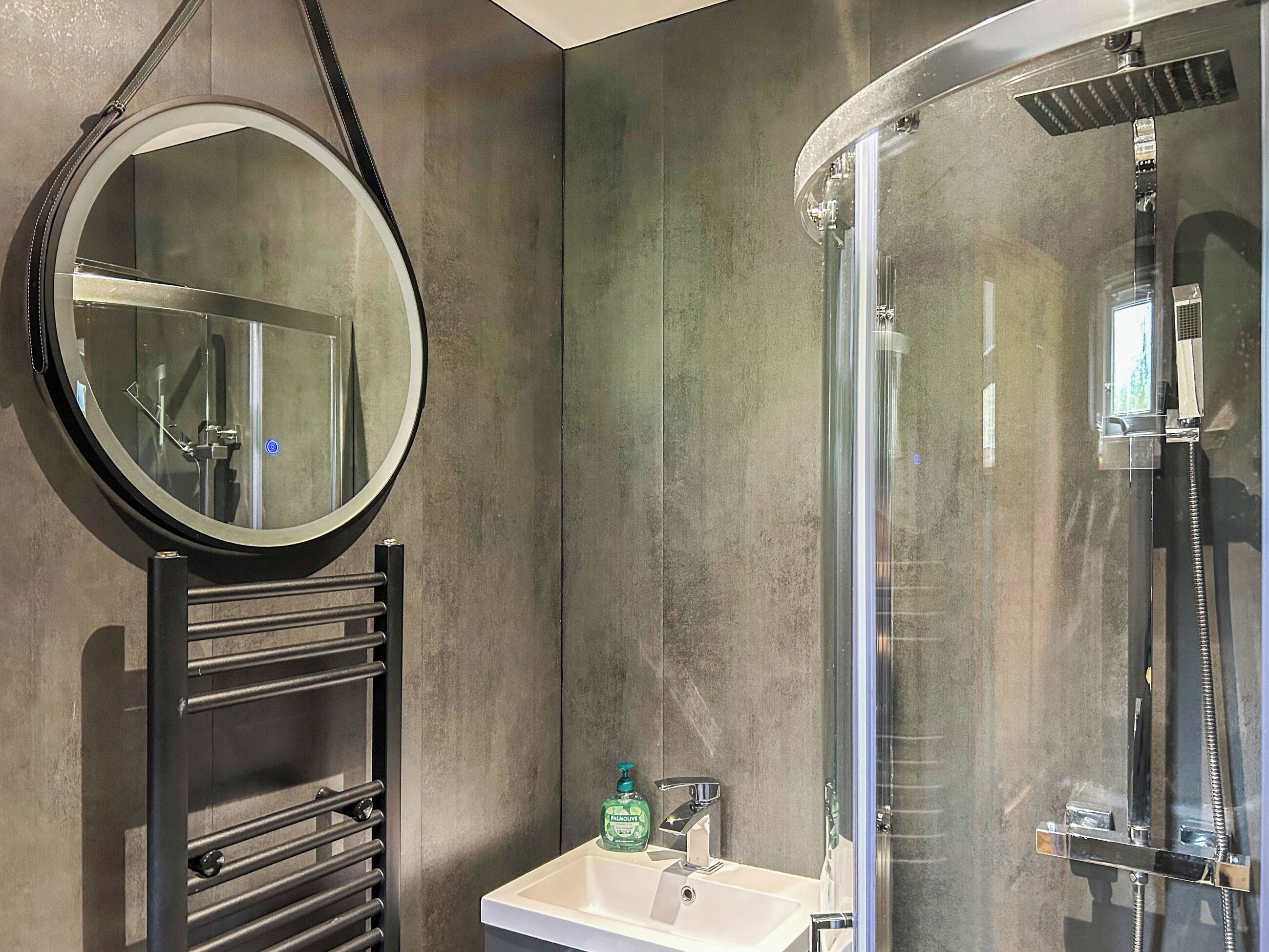 A modern bathroom with a round mirror, a sink, and a glass-enclosed shower.