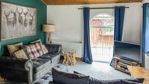 A living room with a sofa, a TV, a radiator, and a window with curtains. - 3 bedroom accommodation in Rothbury (Rothbury)