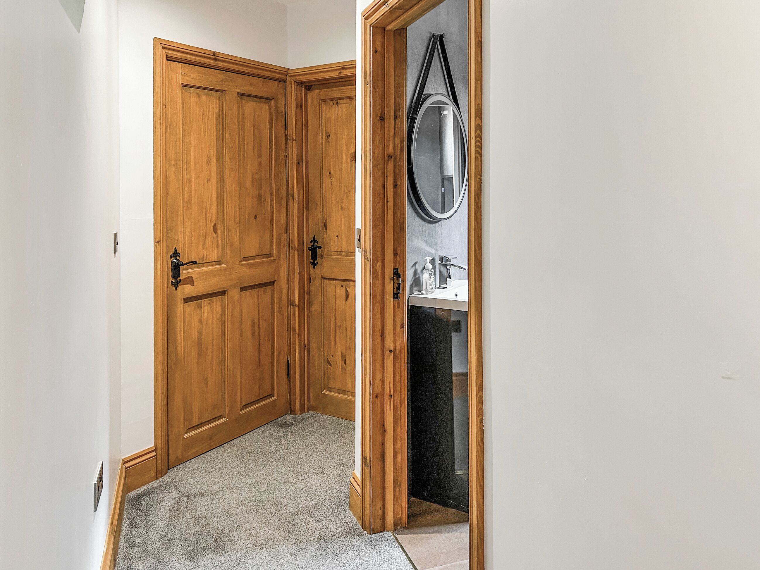 Un pasillo con puertas dobles de madera, un espejo y un lavamanos con artículos de tocador.