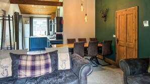 A cozy living room with a sofa, a dining table with chairs, a kitchen in the background, and a wooden ceiling. - 3 bedroom accommodation in Rothbury (Rothbury)