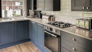 A modern kitchen with dark cabinetry, a stainless steel range, an oven, and a toaster. - 3 bedroom accommodation in Rothbury (Rothbury)
