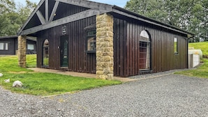 A rustic building with a stone foundation and wooden siding, featuring a prominent entrance and large windows. - 3 bedroom accommodation in Rothbury (Rothbury)