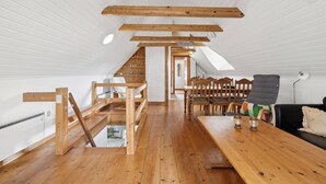 Ein Loft-Zimmer mit freiliegenden Holzbalken, einer Holzbank, einem Esstisch und einem schwarzen Sofa.