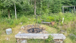 A rustic outdoor setting with a fire pit surrounded by rocks and logs, a wooden bench, and a birdhouse in a forested area. - Stunning home in Skillingaryd with sauna (Skillingaryd)