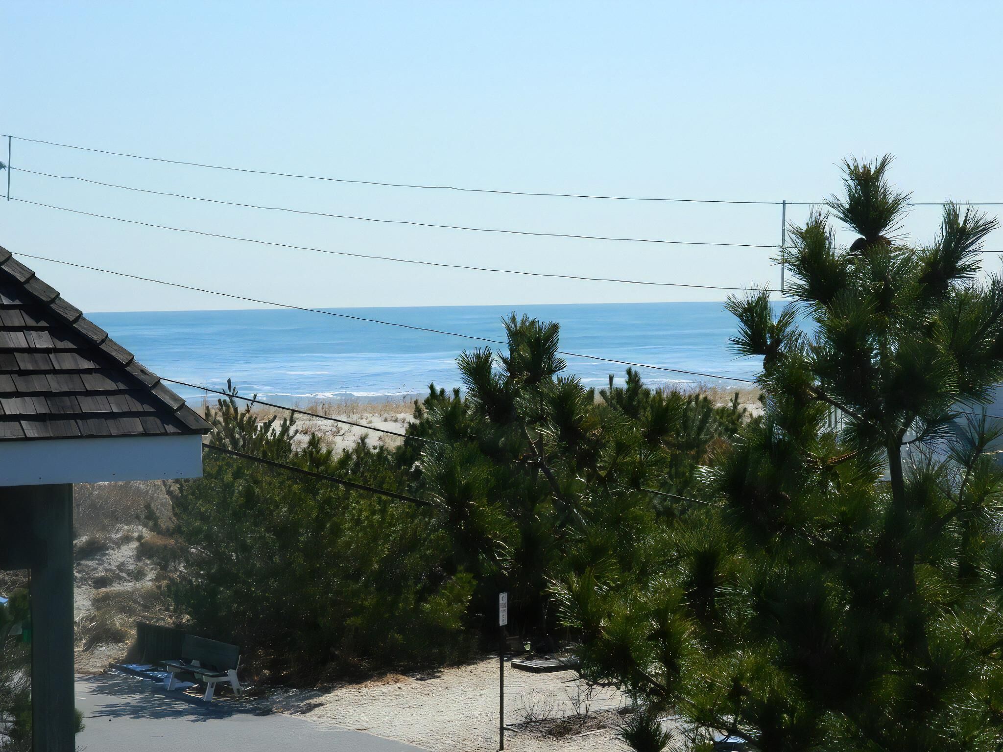 A beach view with a building in the foreground, a clear sky, and power lines overhead.