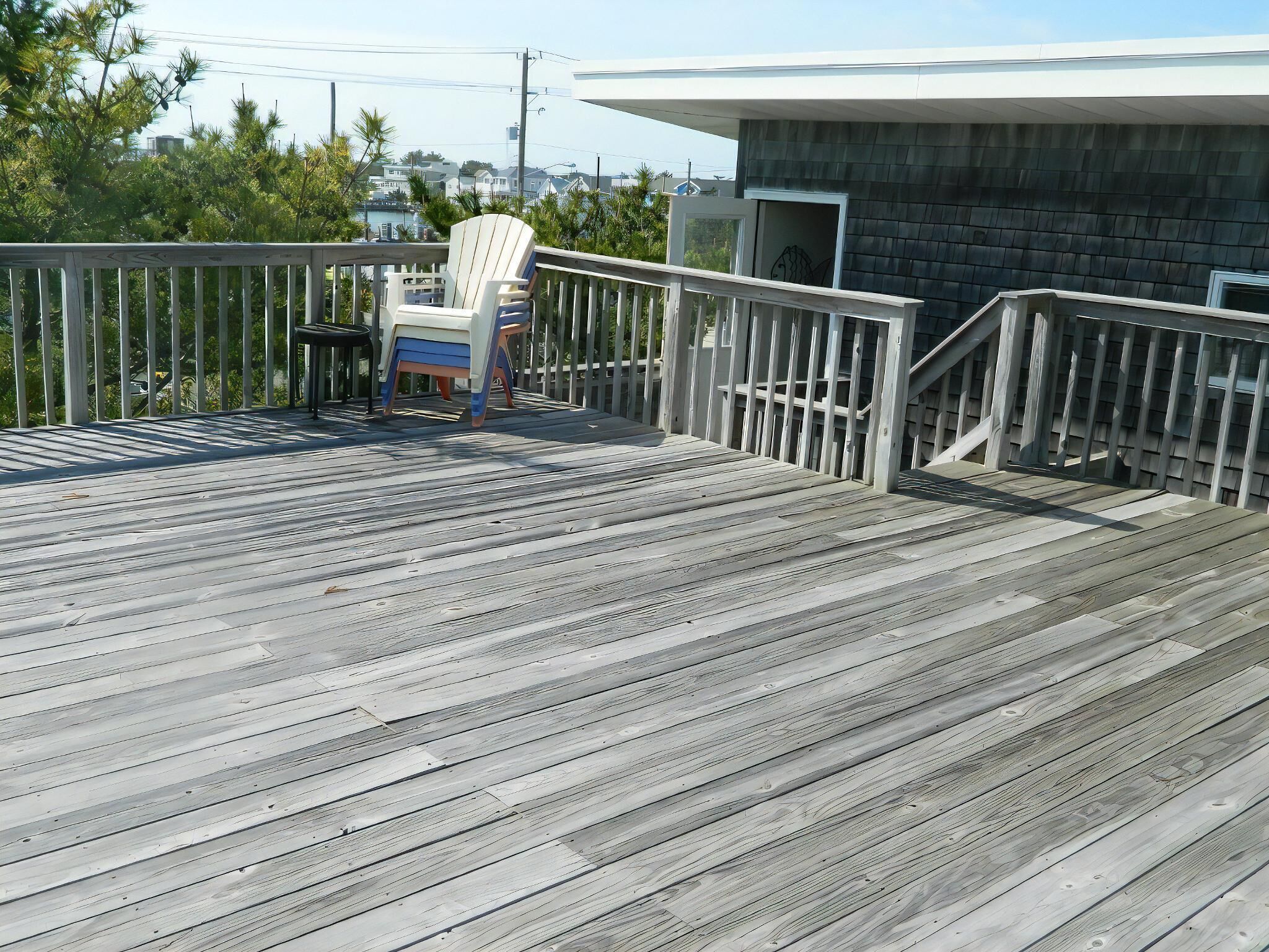 A wooden deck with a white chair, a railing, and a building in the background.