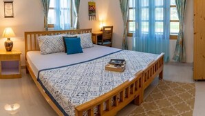 Ein Schlafzimmer mit einem hölzernen Bett, einem gemusterten Bettbezug, zwei Nachttischlampen und Vorhängen.