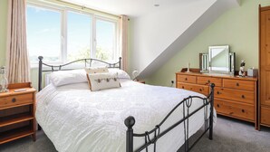 A bedroom with a bed, wooden dresser, and a large window with curtains.