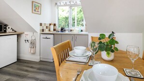 A modern kitchen with white appliances, a dining table set with white dishes, and a window with a view of greenery.