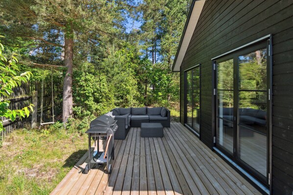 A deck with a sectional sofa, a grill, and a glass-enclosed patio.