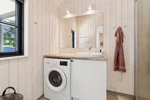 Ett litet badrum med tvättmaskin, handfat och handdukshängare.