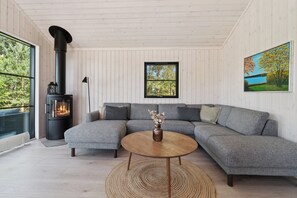Una sala de estar moderna con un sofá seccional, una mesa de centro redonda de madera, una chimenea y un cuadro en la pared.