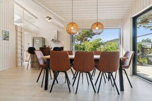 A modern dining area with a large table, multiple chairs, and hanging light fixtures.