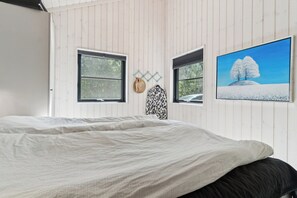 A bedroom with a bed, two windows, a wall-mounted hat rack, and a framed picture.