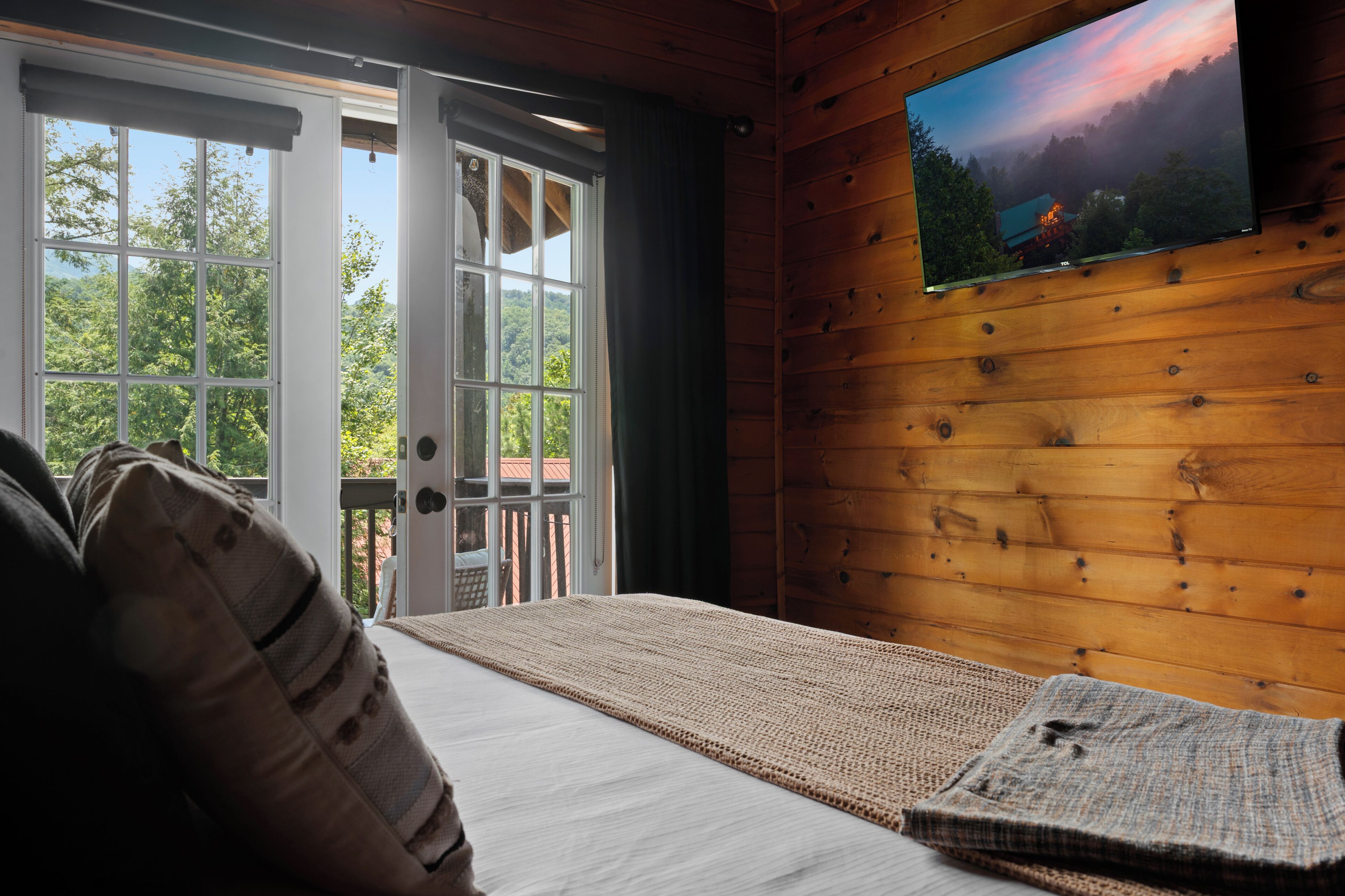 Una habitación con una cama, un televisor montado en la pared y vistas al exterior a través de una puerta.