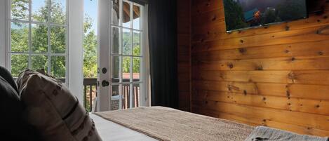 Una habitación con una cama, un televisor montado en la pared y vistas al exterior a través de una puerta.