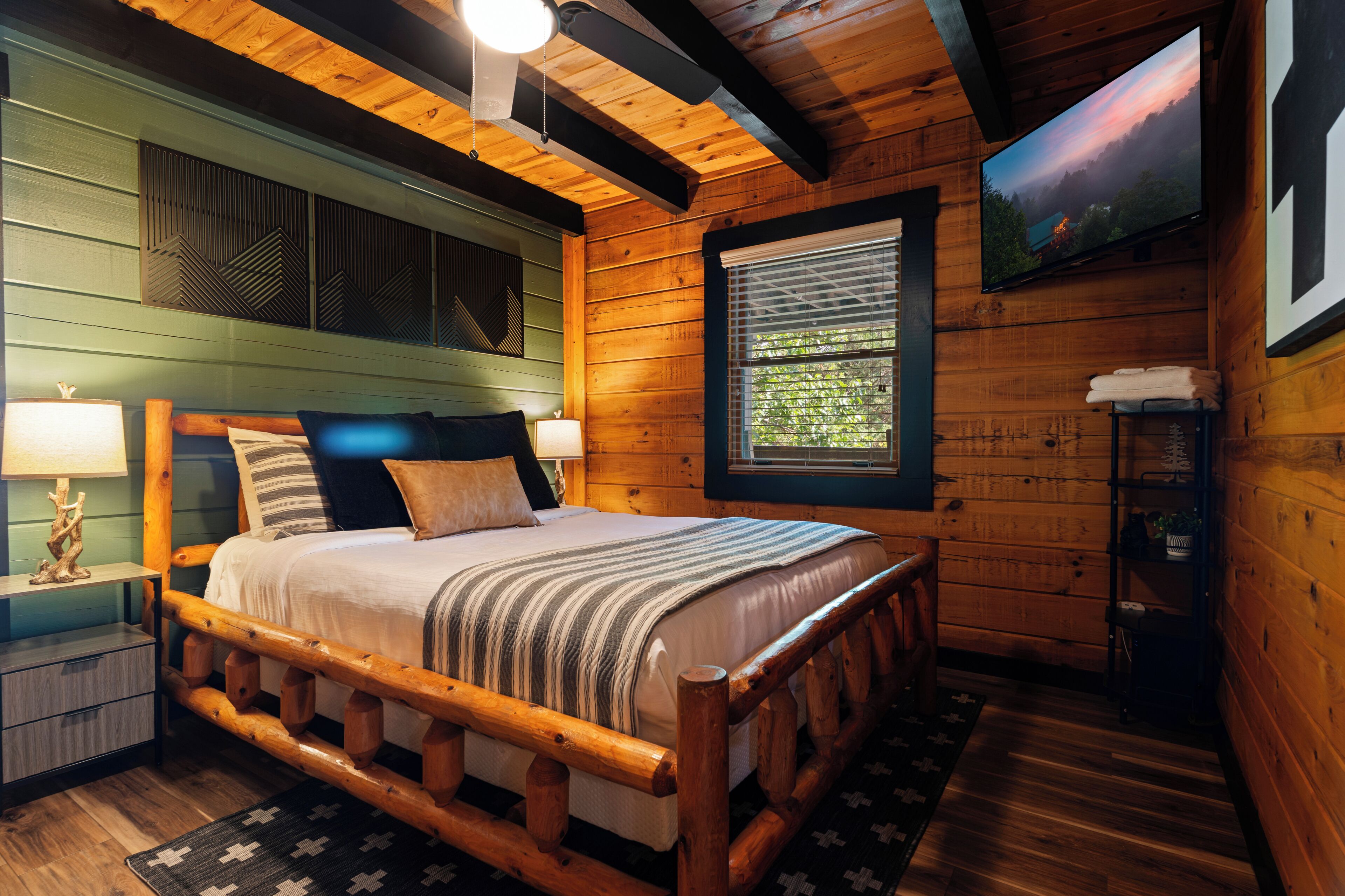 Een slaapkamer met houten wanden, een bed, nachtkastjes, een raam met zonwering en een televisie aan de muur.